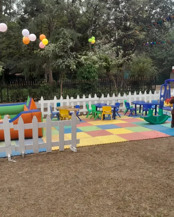 A complete kids' play zone set up outdoors, featuring soft interlocking floor mats, a white picket fence for safety, a ball pool, ride-on toys, and kid-sized tables and chairs.