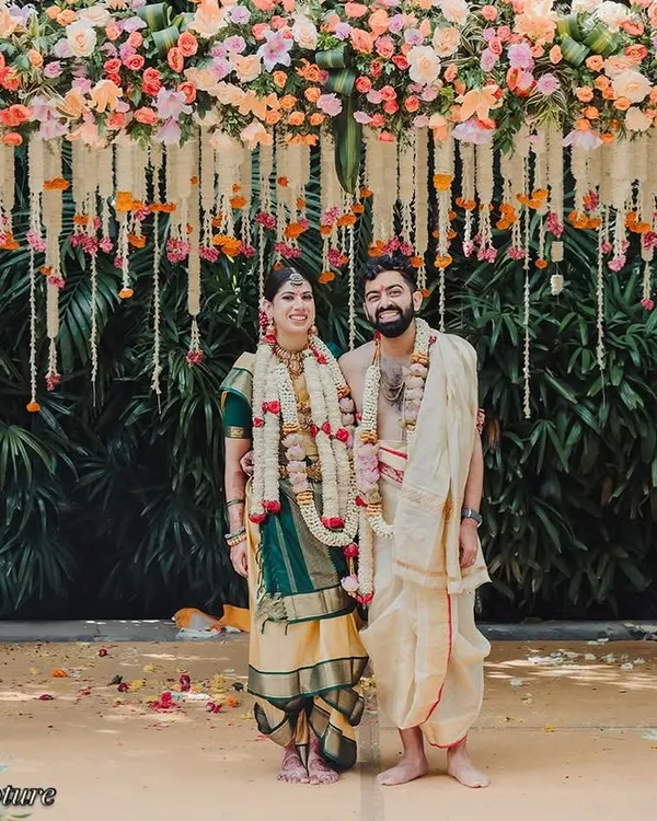 A classic portrait of the couple at their South Indian wedding mandap. The structure is beautifully decorated with colorful flowers and traditional elements, creating a perfect frame for this timeless photograph.