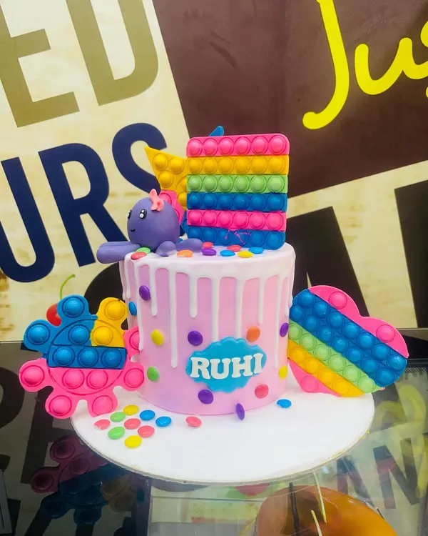 A vibrant 3kg Pop It theme cake, featuring edible, rainbow-colored Pop It toys and a fun drip effect.