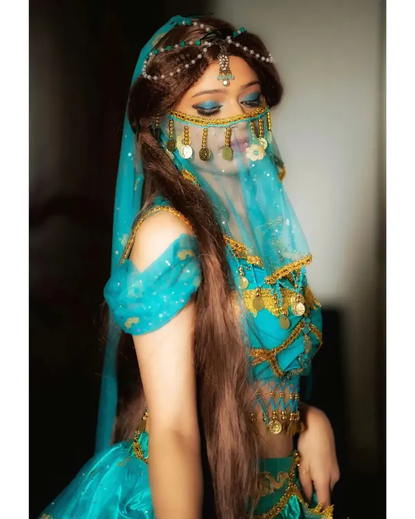 A full view of the Princess Jasmine cosplay. The makeup, featuring shimmering blue eyeshadow and winged liner, is paired with the character's signature costume and accessories for a complete transformation.