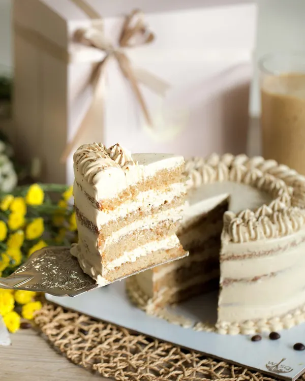 When cold coffee meets cake. This is our Vanilla Latte Cake, featuring moist vanilla cake infused with rich coffee and layered with a homemade coffee mascarpone frosting. A slice is being lifted to show the beautiful layers inside.