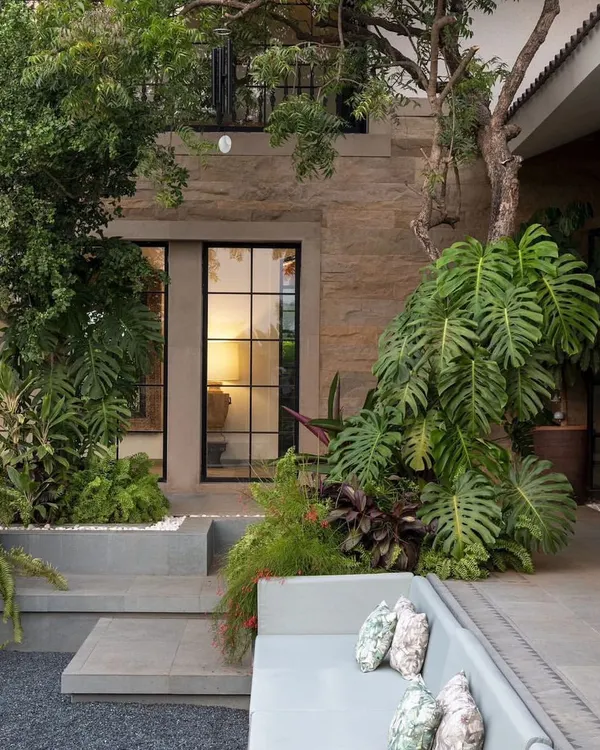 In this Alibaug home, I designed a sunken outdoor lounge surrounded by lush greenery. The built-in seating is nestled amongst large Monstera plants and ferns, creating a private, cozy nook that feels completely immersed in nature.