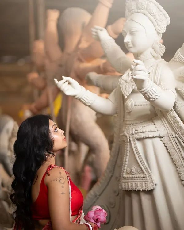 A creative shot from a Durga Puja themed shoot. The makeup is soft yet defined, with an emphasis on the eyes looking towards the divine idol, creating a narrative of devotion and grace.
