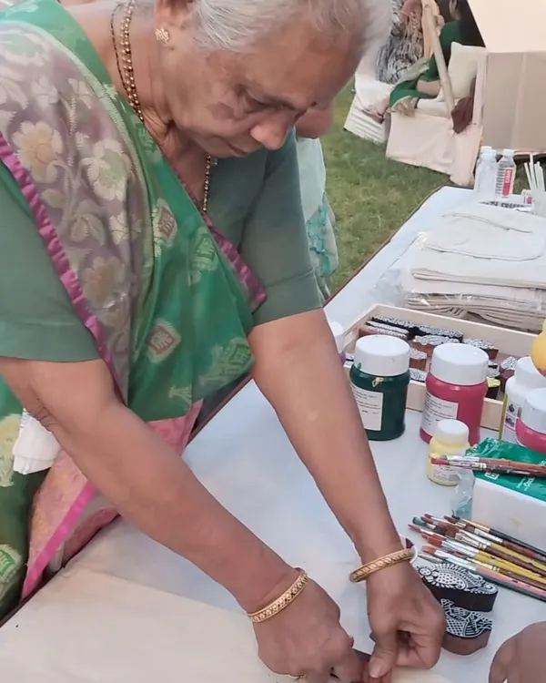 An elderly guest at a pre-wedding event carefully uses a stamp to add a design to a tote bag. Our art corners are designed to be accessible and enjoyable for guests of every generation, adding a unique touch to any celebration.