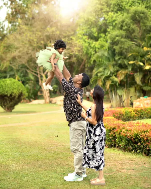 A father joyfully lifts his daughter into the air during a sun-drenched outdoor family session in a park, capturing a perfect moment of pure happiness.
