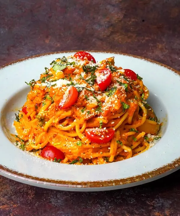 A beautiful plate of spaghetti in a vibrant red sauce, garnished with cherry tomatoes and parmesan. The dark, moody background makes the red of the sauce and tomatoes incredibly rich and appealing.