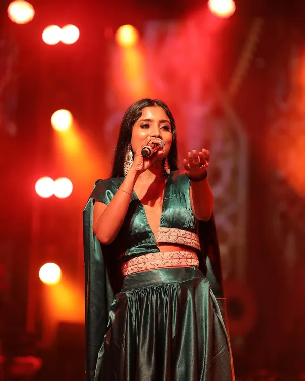 Singer Divya Ramachandra looks stunning on stage in this custom-designed emerald green Indo-western outfit. The crop top with an attached cape and the flowing satin skirt are designed for performance and movement.