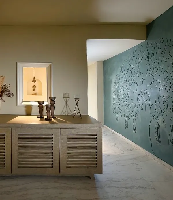 In this Delhi home, we used a deep teal lime plaster to create a feature wall embossed with a 'Tree of Life' motif. This artistic element greets you at the entrance, setting a tone of gentle harmony that flows through the rest of the living spaces.