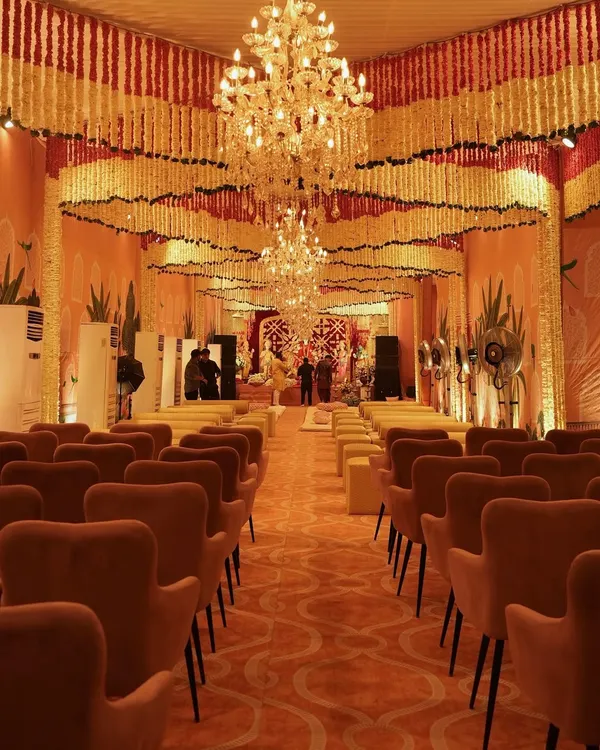 A grand hall prepared for a traditional ceremony, with the ceiling covered in thousands of cascading marigold and tuberose garlands. The opulent crystal chandeliers add a touch of modern luxury to the sacred space.