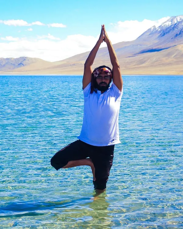 Embodying balance with a Vrikshasana (Tree Pose) in the crystal-clear waters of Pangong Lake. Practicing yoga in nature, surrounded by the majestic Himalayas, is a truly spiritual experience.