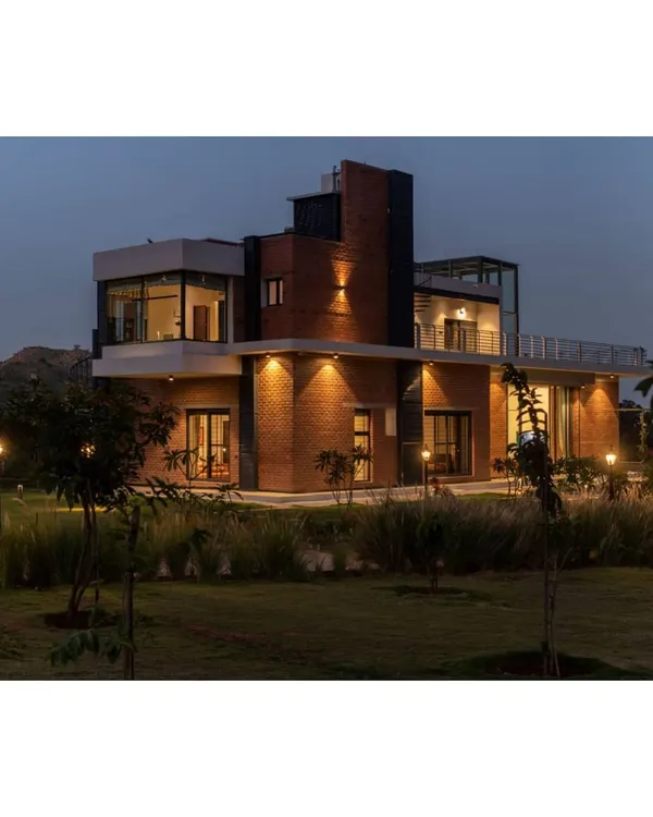 The Weekend Home at Nandi Hills, illuminated at dusk. The design uses warm exterior lighting to highlight the brick texture and create a welcoming glow, settling the structure beautifully into its 3-acre landscape.