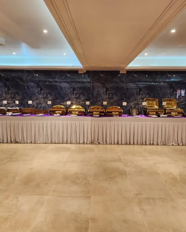 A wide view of a complete banquet setup in a spacious hall. The long, continuous buffet line with gleaming gold chafing dishes creates a grand and inviting look for any large scale event.