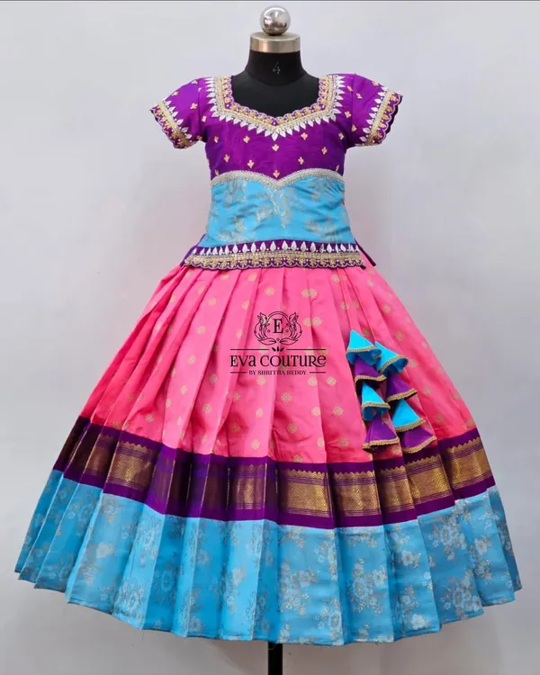 A colorful pattu pavadai with a multi-layered skirt in pink and blue. The purple peplum top has delicate embroidery, tying the colors together.