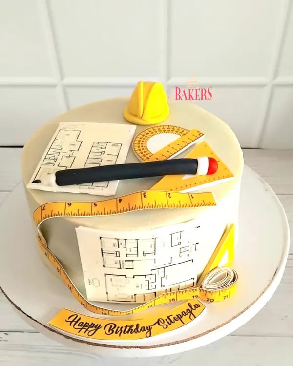 An architect-themed cake for Sitapagl's birthday. This design features edible blueprints, a hard hat, and drafting tools like a protractor and ruler, all handcrafted with great detail.
