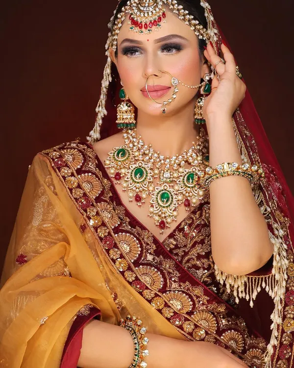This is the quintessential classic bridal look we are celebrated for. It features a flawless base, dramatic smokey eyes with a hint of glitter, and bold lips, all perfectly complementing the rich maroon and gold lehenga and heavy kundan jewelry. This look is designed for the bride who wants to feel like royalty on her wedding day.