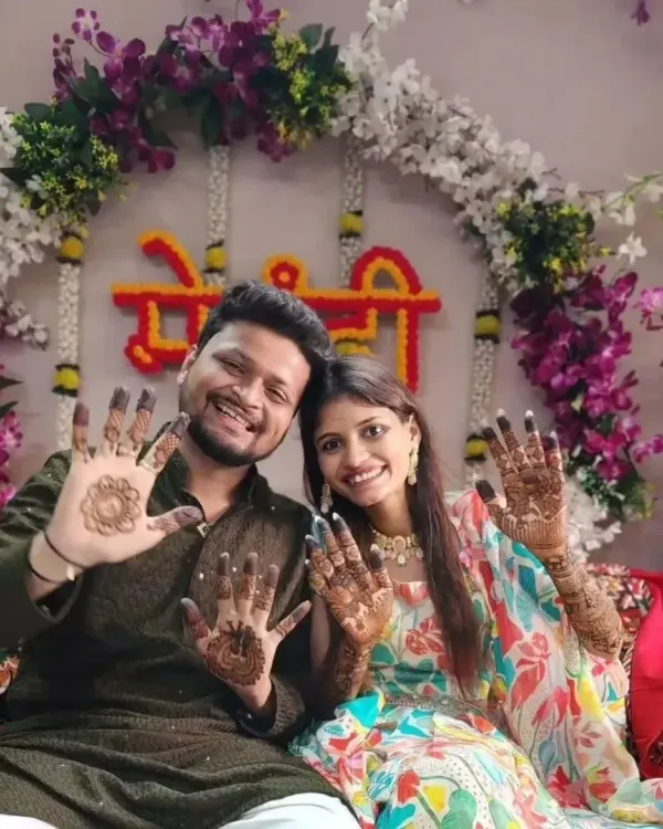 A happy couple proudly showing their mehandi designs during their celebration. The groom has a simple mandala, while the bride has intricate patterns on her palms.