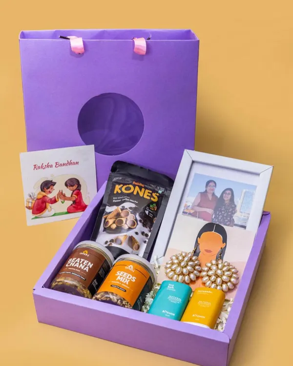 This Rakshabandhan hamper is a perfect example of a complete gift set. It includes a personalized photo frame, healthy snacks, traditional earrings, and a Rakhi card, all beautifully packed in a custom gift bag.