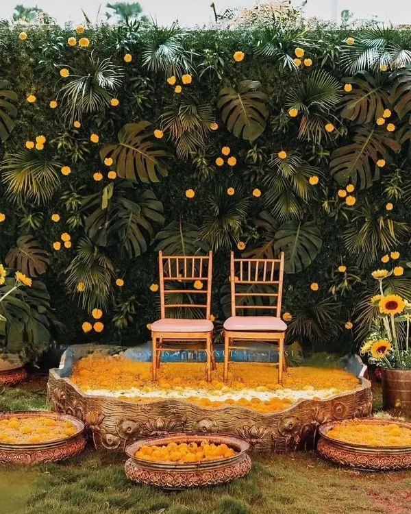 A beautiful Haldi setup combining a lush green backdrop of monstera leaves with bright yellow marigolds for a tropical, vibrant feel.