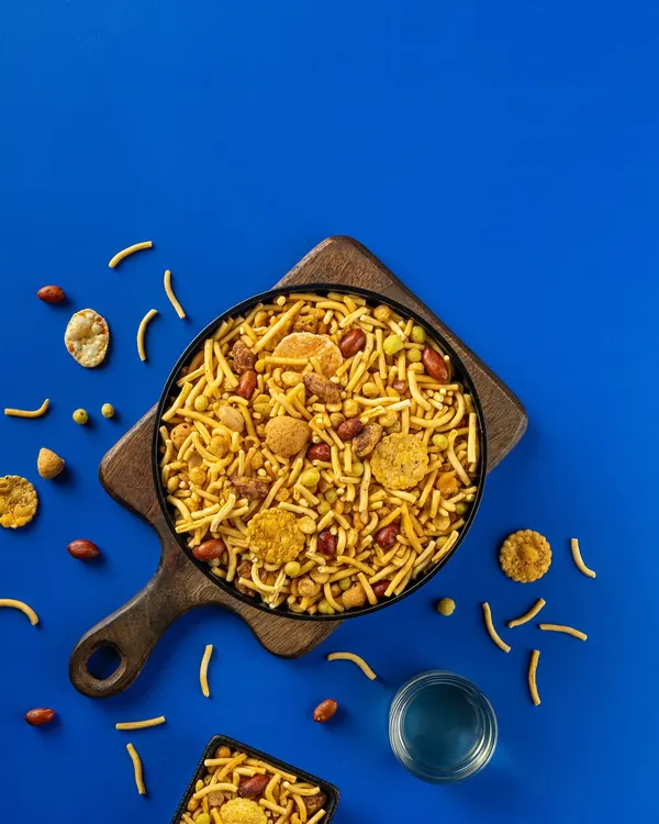 A flat-lay photograph of a savory Indian snack mix for Sartaj Sweets & Namkeen. The bold blue background makes the product pop, a technique I use for effective packaging design.