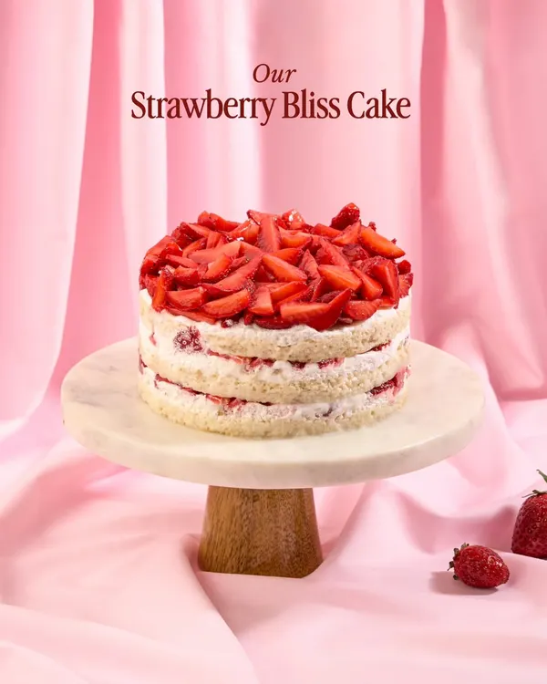 My Strawberry Bliss Cake, showcased on a marble stand. This naked-style cake features layers of fluffy vanilla sponge, fresh cream, and is generously topped with chopped strawberries.
