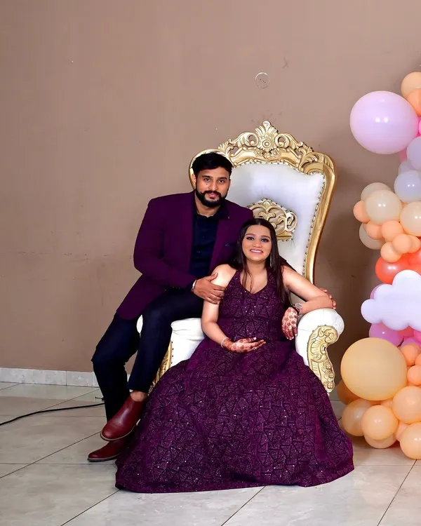 The happy couple seated on a classic white and gold throne chair, ready to celebrate their upcoming arrival in front of our custom decor.