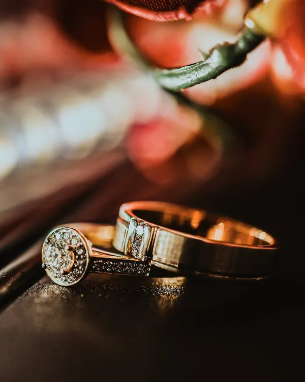 A stunning macro shot of the wedding rings, resting on a dark surface with a warm, colorful bokeh background. This artistic photo turns the symbol of your union into a beautiful work of art.