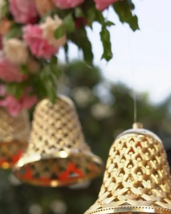 A close-up of decorative golden bells hanging amidst a floral arrangement. These small, traditional details add a touch of elegance and a gentle sound to the wedding atmosphere.