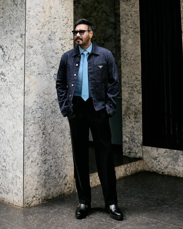 A full-length view of Ajay Devgn's Prada look, showing the perfect pairing of the denim jacket with black trousers and chunky dress shoes.