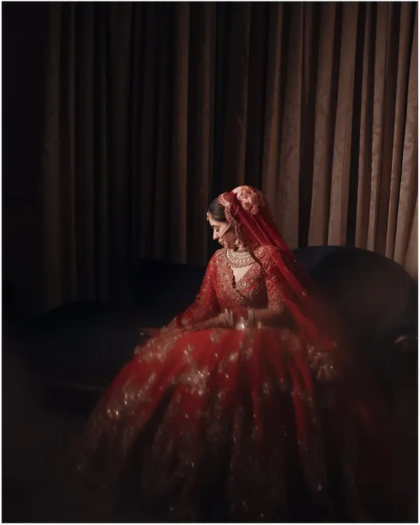 A bride in her full glory. This portrait of Anshika in her stunning red lehenga uses dramatic, low-key lighting to create a sense of timeless elegance and quiet contemplation.