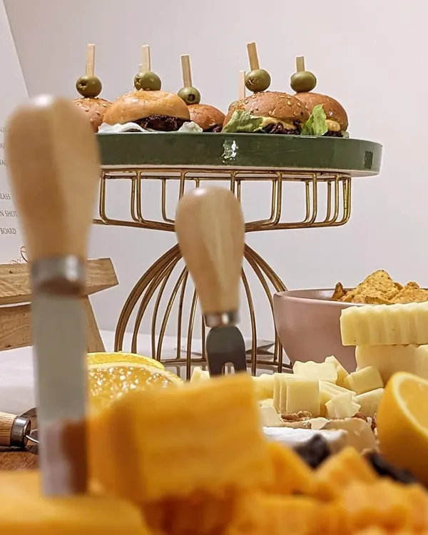 A glimpse of a multi-level setup, with mini burgers on a raised platter above a board of artisanal cheeses. I use height and texture to create visually dynamic spreads.