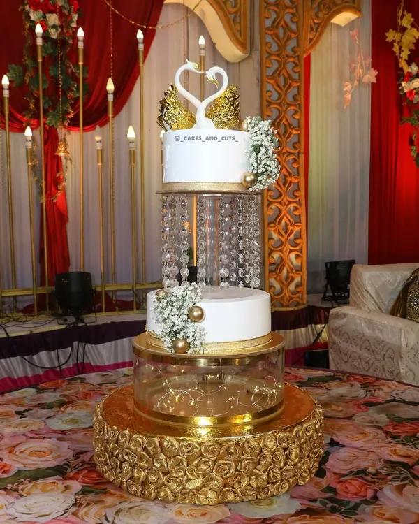 A beautiful three-tier engagement cake featuring crystal chandeliers and elegant swan toppers, set up at a grand venue. We show you how to assemble these showstoppers on-site.