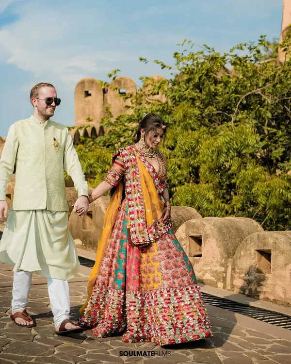 A beautiful shot of a couple in vibrant, traditional attire walking hand-in-hand along a historic fort wall. This image captures the essence of a royal Rajasthani pre-wedding shoot, filled with color and heritage.