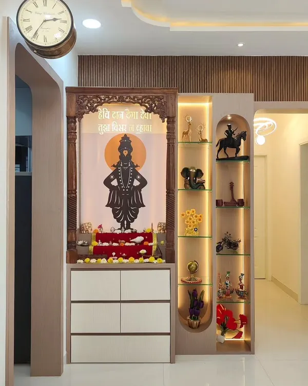 This pooja unit is designed as a statement piece, featuring a traditionally carved wooden frame around a backlit panel. It includes drawers for storage and an illuminated glass cabinet on the side for displaying religious artifacts.