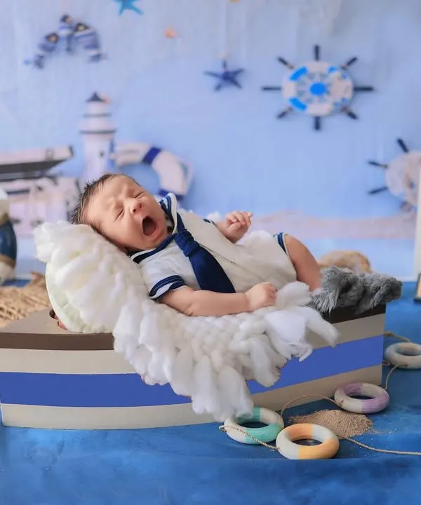 Ahoy, little sailor! This newborn is captured mid-yawn in a boat-shaped prop, surrounded by a complete nautical set with anchors, lifebuoys, and a lighthouse.