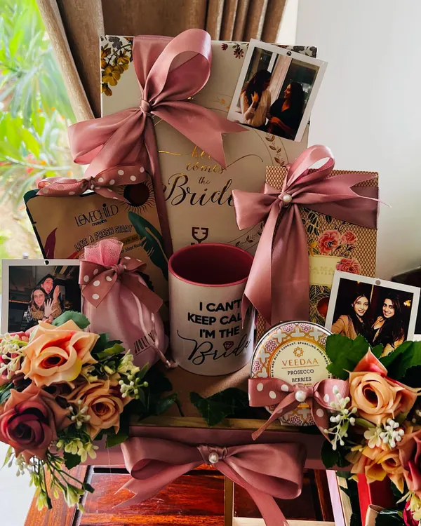 A closer look at the top tier of the personalized wedding hamper, showcasing a custom 'Here Comes the Bride' box, a fun mug, and photos of the bride with her friends, all adorned with beautiful silk flowers.