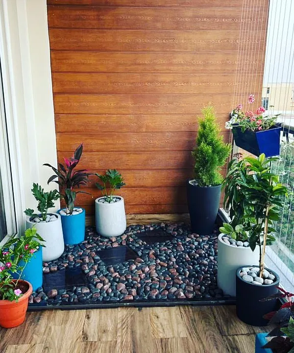 A beautiful balcony setup combining pebble flooring with a variety of potted plants. We used a mix of planters and a wooden accent wall to create a cozy, stylish corner perfect for enjoying a morning coffee.