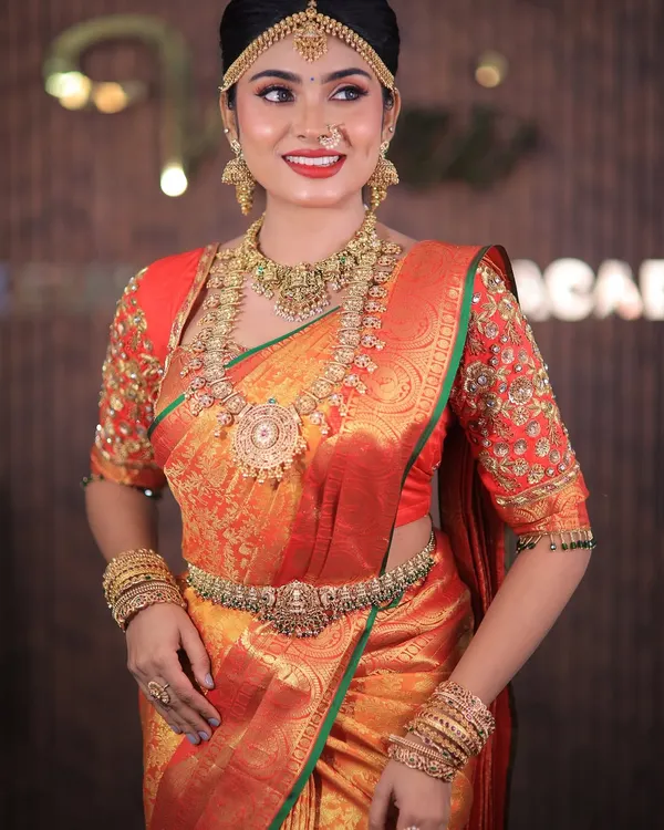 This is the classic South Indian Muhurtham look that I absolutely love creating. The rich red and gold Kanchipuram silk is draped to perfection, with sharp pleats and a secure fit, ensuring the bride looks and feels like a queen on her big day.