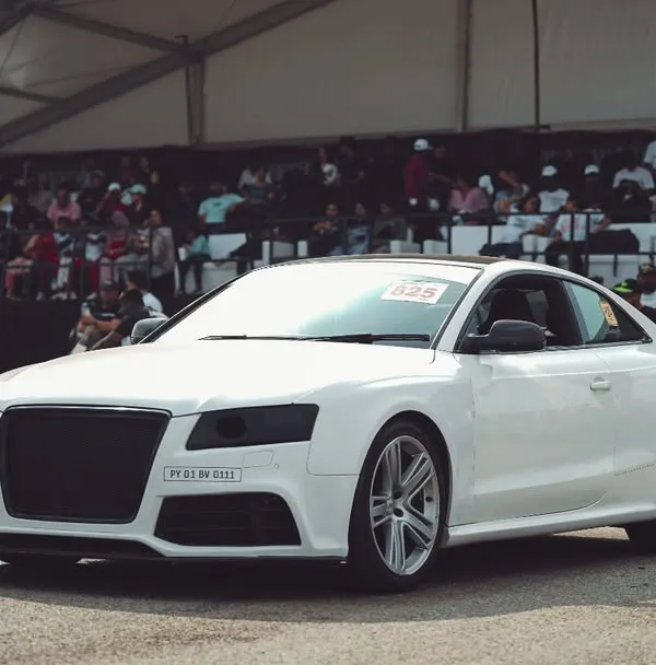 A white Audi A5 coupe at the starting line, with the packed grandstand in the background. This is where performance meets a passionate audience.