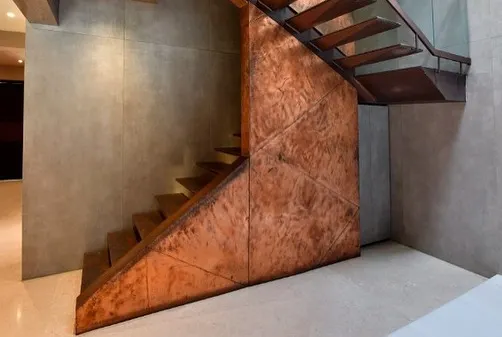 This copper and metal staircase at a Sainik Farms residence is designed as a sculptural element. The cantilevered treads create a sense of lightness, while the textured copper cladding adds warmth and intensity, heightening the sense of ascent.