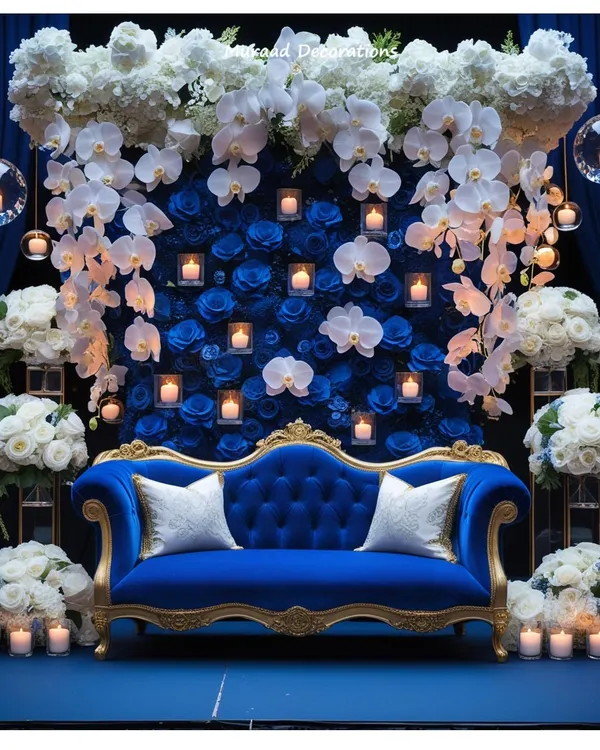 This royal blue and gold stage is one of my signature looks for a truly luxurious reception. I combined a wall of deep blue roses with cascading white orchids and dozens of floating candles to create a dramatic, photo-ready backdrop. The velvet couch adds that final touch of regal comfort for the couple.