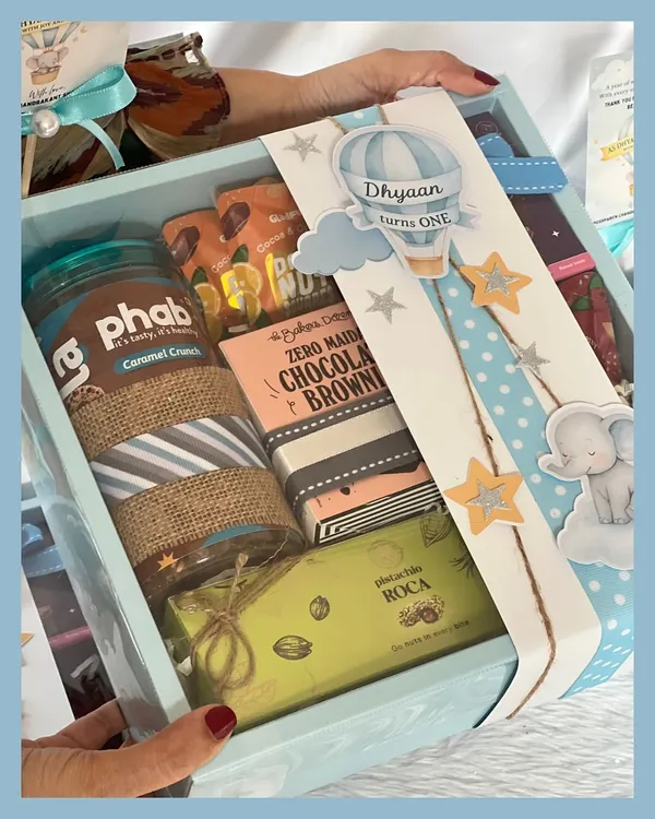 A closer look at our hot air balloon and elephant themed first birthday hamper. It’s filled with goodies like a granola jar, chocolate brownies, and pistachio roca, all wrapped with a custom sleeve.