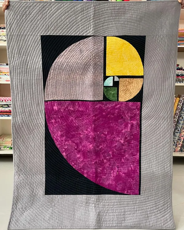 A magnificent art quilt depicting the Fibonacci spiral. The design is enhanced by quarter-inch spiral quilting that radiates outwards, creating a mesmerizing visual effect.