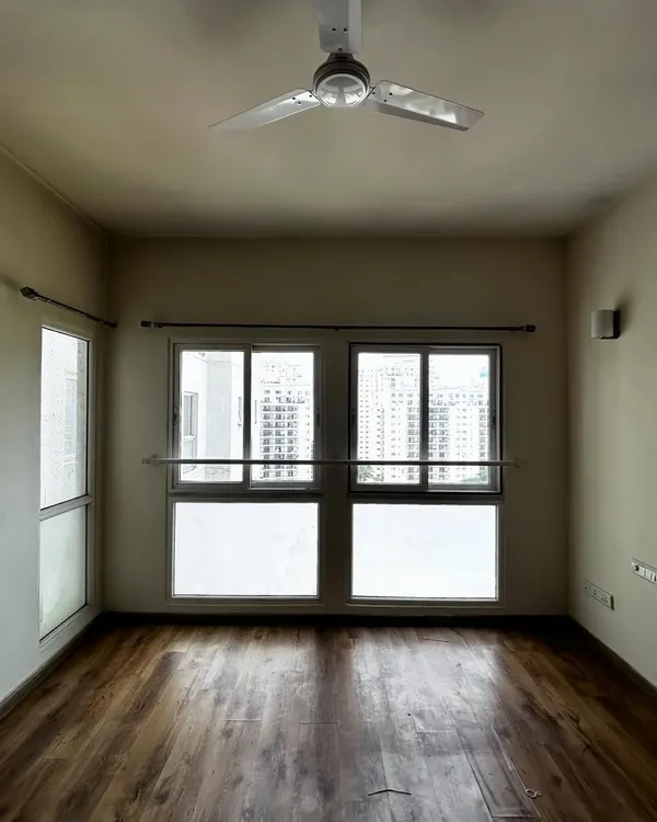 Before: An empty guest room in the 'Cover me in Sunshine' project, with standard windows and wooden flooring, waiting for a touch of warmth and functionality.