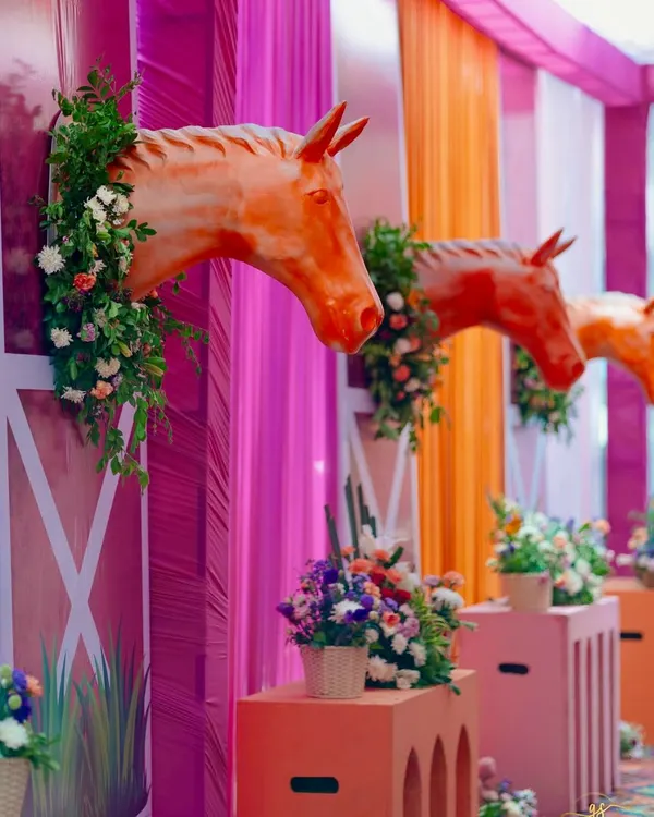 A close-up of the equestrian-themed Haldi decor, where horse-head sculptures emerge from vibrant pink stable-like walls, adorned with fresh flowers.