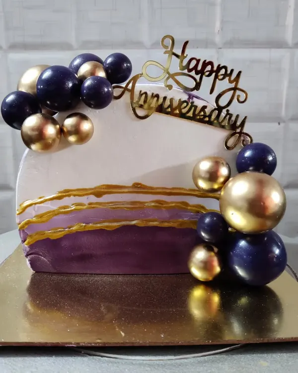 A modern and stylish anniversary cake. This unique design features a half-cake shape with purple and gold spheres and abstract gold lines.