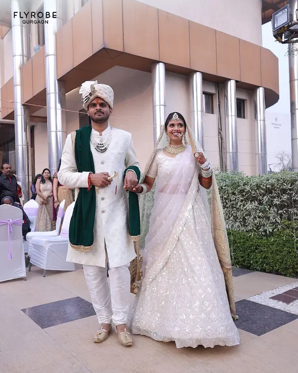 Make a grand entrance together. This couple looks absolutely regal, with him in a classic white sherwani with a contrasting green stole and her in a delicate white chikankari lehenga. A perfect look for a day wedding.