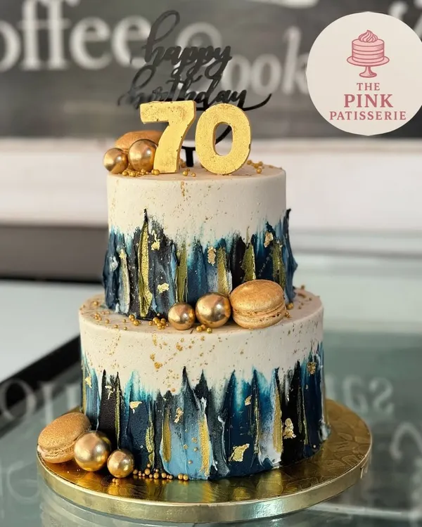 A striking two-tiered cake for a 70th birthday. This modern design features a brushed blue and gold effect, accented with gold macarons, spheres, and a bold "70" topper.