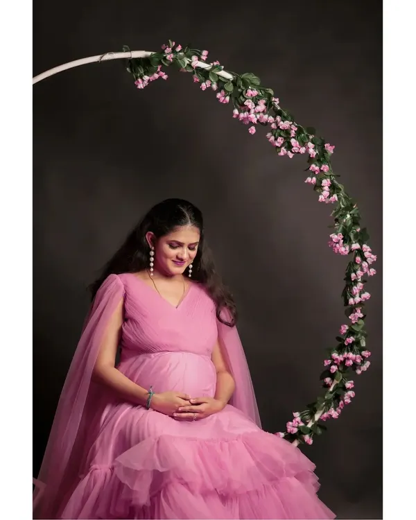 A serene solo portrait of the mother-to-be in our pink ruffle gown. The floral ring prop frames the shot beautifully against a simple dark backdrop.