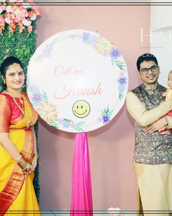 A beautiful family portrait from a naming ceremony. The proud parents pose with their newborn next to a custom sign announcing the baby's name.