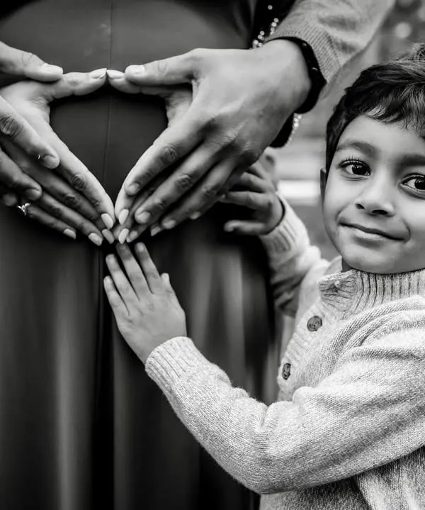 A beautiful black and white portrait showing the hands of the parents and older brother forming a heart on the baby bump. This is a powerful symbol of a family's love and anticipation.